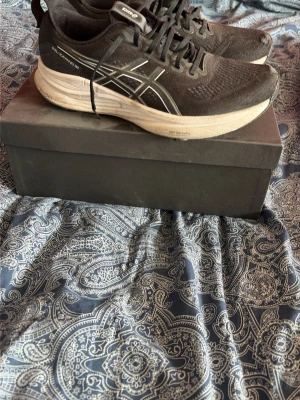 Asics skor - Säljer ett par svarta Asics sneakers med vit sula och klassisk logga på sidan. Skorna har mesh-ovandel för bra ventilation och svarta snören. Perfekta för dig som gillar sportig stil och komfort.