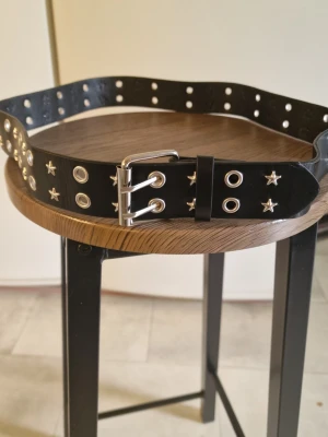 Skärp nitar svart - Skärp nitar svart. Nitbälte för kvinnor. Justerbart brett svart bälte med metallspänne. 109 cm. Bredd 3,8 cm.