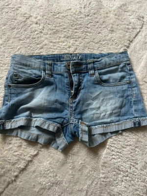 Blå jeansshorts med uppvik - Snygga blå jeansshorts med uppvikta benslut och klassisk femficksdesign. Shortsen har bälteshällor, knapp och dragkedja framtill. Perfekta för varma dagar och ger en avslappnad look.