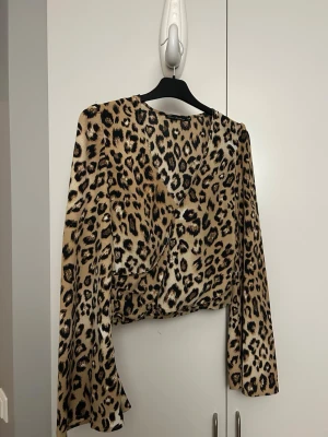 Leopardmönstrad omlottopp med långa ärmar - Snygg leopardmönstrad omlottopp med långa ärmar och croppad passform. Toppen är V ringad och i väldigt fint skick. Denna är från NLY Trend 
