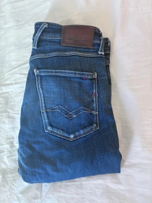 Replay mörkblå - Snygga mörkblå jeans med klassiska fem fickor och kontrastsömmar. Jeansen har en skinnpatch i midjan och diskreta slitningar för en trendig look. Tillverkade i stretchig denim för extra komfort.