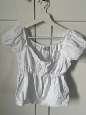 Vit puffärmad blus med resår - Söt vit blus med puffärmar och resår i midjan samt vid halsringningen. Blusen har en lätt v-ringad form och är tillverkad i ett tunt, luftigt material som passar perfekt till sommaren. Enkel att styla med både jeans och kjol.