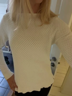 Vit strukturerad stickad tröja - Säljer en vit stickad tröja med snygg struktur och rund hals. Tröjan har långa ärmar, ribbade muddar och nederkant samt en liten slits i sidan. Perfekt till jeans eller kjol för en clean look.