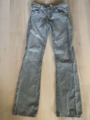 Grå bootcut jeans med knappar - Snygga grå jeans med bootcut-modell och knappgylf. Klassisk femficksdesign och raka ben som blir vidare nedtill. Perfekta för dig som gillar en avslappnad men ändå trendig look. Tillverkade i denim med en lätt tvättad finish.