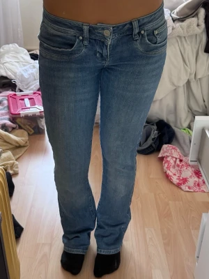 Blå raka jeans med låg midja - Säljer ett par klassiska blå jeans med låg midja och raka ben. Jeansen har fem fickor och stängs med knapp och dragkedja. Materialet är denim i bomull med en lätt tvättad look. Perfekta för en avslappnad och trendig stil. Passar perfekt på 165