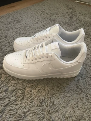 Nike air foce one - Säljer ett par helvita sneakers i klassisk modell med lågt skaft. Skorna har perforerad tå, vita skosnören och sula med bra grepp. Tillverkade i slätt läder med diskreta sömmar och stilren design.