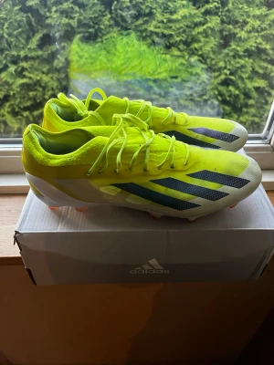 Adidas crazyfast FG elite - Säljer ett par neongula Adidas fotbollsskor med svarta och vita detaljer. Endast använda några gånger och har bytt helt nya sulor också. Skorna har låg profil, snörning och en lätt ovandel i syntetmaterial. Sulan har fasta dobbar i orange och rosa för bra grepp på gräsplan. Perfekta för dig som vill sticka ut på planen!