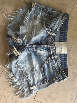 Blå jeansshorts med fransar - Säljer ett par blå low waist jeansshort, storlek 23 -märket one tea spoon.