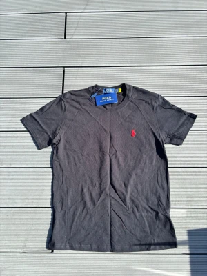 Svart t-shirt från Polo Ralph Lauren - Snygg svart t-shirt från Polo Ralph Lauren med klassisk passform och korta ärmar. T-shirten har en liten röd broderad logga på bröstet och är gjord i mjuk bomull. Perfekt till jeans eller shorts. Skulle säga den passar mer åt S 