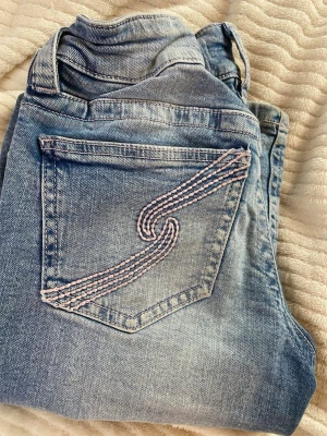 Ljusblå jeans från Gina Tricot - Säljer ett par ljusblå jeans från Gina Tricot med snygg slitning och broderad bakficka i rosa och vitt. Klassisk femficksmodell med knapp och dragkedja. Perfekta till en avslappnad look och passar till det mesta i garderoben.
