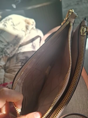 Pink Beige michael kors  handväska med guldiga dragkedjor - Snygg beige handväska i läderimitation med två stora fack och guldiga dragkedjor. Väskan har justerbar axelrem och ljus insida med quiltat mönster. Perfekt för dig som vill ha en stilren och praktisk accessoar.