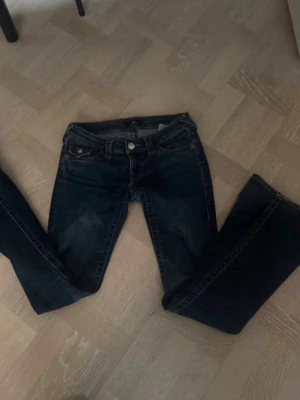  True Religion jeans joey - Säljer ett par mörkblå jeans från True Religion med klassiska kontrastsömmar och ficklock bak. Modellen har bootcut och detaljerade bakfickor.De har lite missfärgning som man kan se men när man har på sig dom är de inget man ser eller tänker på.Säljer för ett dunder pris för 600kr!!Skriv om de har några  frågor 