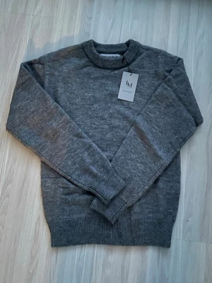 Grå stickad tröja från Ivan March - Mysig grå stickad tröja från Ivan March med rund halsringning och ribbade muddar vid ärmslut och nederkant. Perfekt för lager på lager och enkel att matcha med olika outfits. Materialet ser ut att vara mjukt och bekvämt.