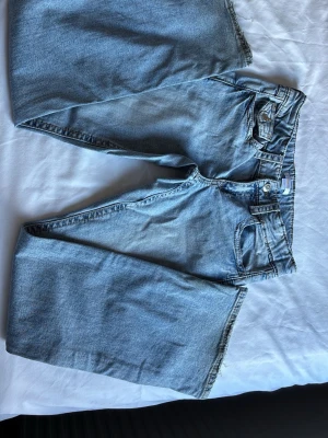 Ljusblåa flared jeans med fransig kant - Säljer ett par ljusblå jeans med flared passform och fransig kant nedtill. Jeansen har klassisk femficksdesign och en snygg ficka med lock bak. Perfekta för en avslappnad och trendig look.