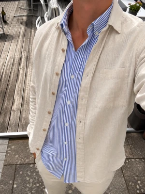 Beige/cream linne overshirt Massimo Dutti - Säljer en stilren beige/cream overshirt från Massimo Dutti i 100% linne.  Overshirten har klassisk krage, bröstficka och knappar framtill. Den är perfekt att bära över en skjorta eller T-shirt och passar lika bra till jeans som shorts.  Storlek: S Material: 100% linne Färg: Beige/Cream  Hör gärna av dig vid frågor eller funderingar! 📩