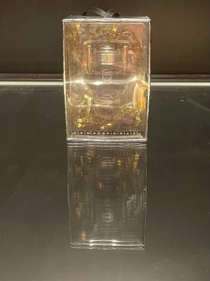 Paco Rabanne parfymflaska - Säljer en parfym från Paco Rabanne i en unik, genomskinlig flaska formad som en pokal med silverfärgade detaljer. Flaskan kommer i en genomskinlig förpackning med guldfärgade dekorationer. Perfekt för dig som gillar exklusiva och snygga parfymer.