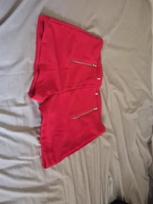 Röda shorts med dragkedjor - Snygga röda shorts med två dekorativa dragkedjor framtill. Modellen är kort och har en enkel, clean design utan mönster. Perfekta för varma dagar och ger en färgklick till din outfit. Vet inte storleken då lappen blivit bort klipt