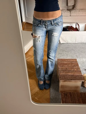 Ljusblå slitna bootcut jeans - Säljer ett par ljusblå bootcut jeans med slitna detaljer. Har varit mina favorit jeans och är därför väldigt andvända. De har ett litet hål under rumpan som inte syns. Säljer då de inte längre kommer till användning.