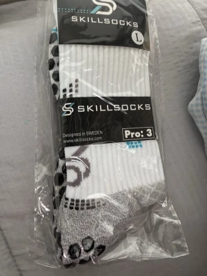 Vita sportstrumpor från Skillsocks pro:3 helt oöppnad - Säljer ett par vita sportstrumpor från Skillsocks, modell Pro:3. Strumporna har svarta och grå detaljer samt halkskydd under foten. Perfekta för träning och sport. Designade i Sverige och tillverkade i ett bekvämt material.