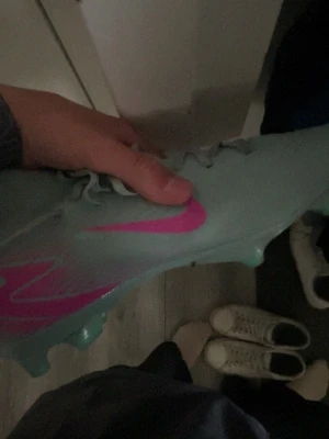 Ljusblåa fotbollsskor med rosa detaljer - Säljer ett par ljusblåa fotbollsskor med en stor rosa logga på sidan. Skorna har dobbar för bra grepp på planen och är tillverkade i ett syntetmaterial som ger en tight och smidig känsla på foten. Perfekta för dig som vill sticka ut på fotbollsplanen.