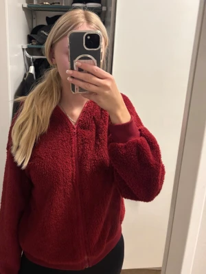 Vinröd teddyjacka med dragkedja - Mysig vinröd teddyjacka med dragkedja framtill och ribbade muddar vid ärmslut och nederkant. Jackan har en fluffig och mjuk textur som ger en avslappnad look. Perfekt för att hålla värmen under kyliga dagar. Vet inte vart den kommer ifrån då de inte finns nån lapp kvar men skulle tippa på shein. 