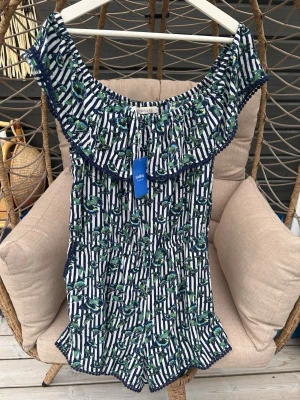 Offshoulder jumpsuit - Säljer en snygg offshoulder jumpsuit från Oasis i storlek XL. Den är marinblå med vita ränder och grönt blommönster, volangkant upptill och är ärmlös. Perfekt för sommarens alla tillfällen!