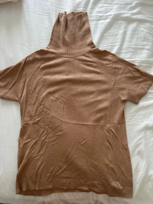 Beige polotröja från MNG - Stickad beige polotröja från MNG med korta ärmar och hög, ribbad polokrage. Tröjan har en mjuk och tunn kvalitet, perfekt för lager på lager och en clean look. Passar till både jeans och kjol för en trendig stil.