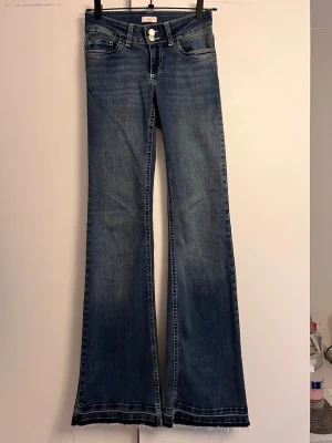 Blå bootcut jeans med broderade fickor - Säljer ett par blå bootcut jeans med rå kant nertill och snygga broderade detaljer på bakfickorna. Jeansen har klassisk femficksmodell, låg midja och är tillverkade i denim med lätt stretch. Perfekta för dig som gillar retrovibbar och markerad siluett.