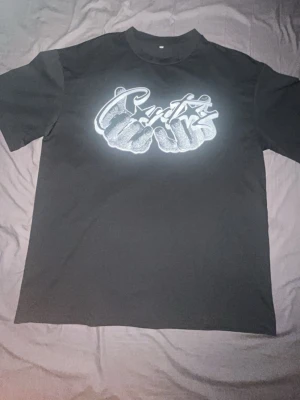 Svart Cortiez T-shirts  - Säljer en svart t-shirt med ett stort grafiskt tryck på bröstet som föreställer två händer och text i streetstil. T-shirten har rund hals och korta ärmar. Perfekt för dig som gillar en edgy och urban look.
