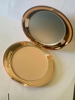 Charlotte Tilbury puderfoundation - Snygg puderfoundation från Charlotte Tilbury i en lyxig, oval guldskimrande dosa med spegel. Färgen är ljusbeige och formulan är pressat puder som ger en naturlig finish. Perfekt att ha i väskan för touch-ups under dagen.