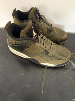 Olivgröna Air Jordan 4 sneakers - Snygga Air Jordan 4 sneakers i olivgrönt mocka och mesh med svarta och vita detaljer. Klassisk siluett med högt skaft, ikonisk Jumpman-logga på plösen och robust sula. Perfekta för dig som gillar streetwear och vill sticka ut med en unik färg.