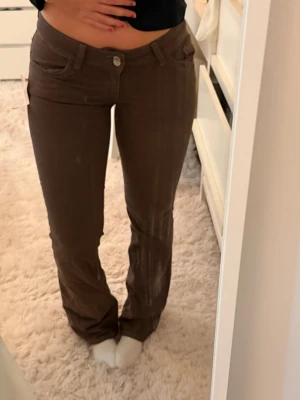 Bruna bootcut jeans med låg midja - Snygga bruna jeans med bootcut-modell och låg midja. Jeansen har klassiska fem fickor och stängs med knapp och dragkedja. Materialet ser ut att vara stretchigt och bekvämt, perfekt för en trendig och avslappnad look. Helt nya med prislappen kvar