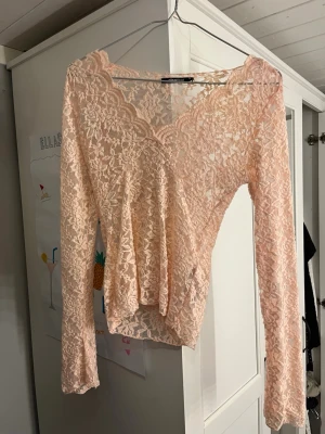 Ljusrosa spetsblus med v-ringning - Säljer en romantisk ljusrosa blus i spets med v-ringad omlottfront och långa ärmar från Gina tricot i xs. Toppen har fina volangdetaljer längs halsringningen och är perfekt för dig som gillar en feminin stil. Använd ett par fåtal gånger satt den är i fint skick 