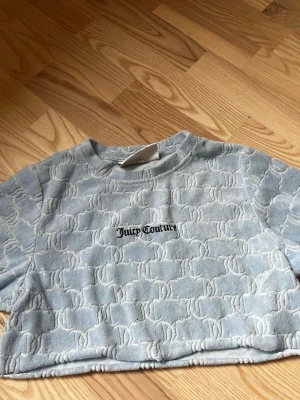 Blå croppad topp från Juicy Couture - Superfin ljusblå croppad topp från Juicy Couture med upphöjt mönster och broderad logga framtill. Mjuk och skön i frotté, perfekt för en chill och trendig look.