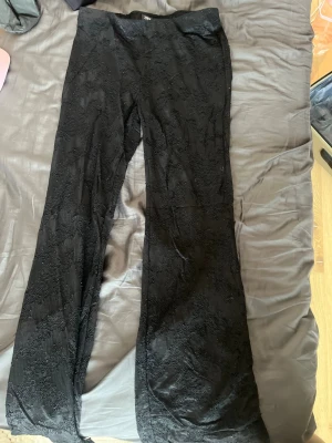 Svarta spetsbyxor från Zara - Säljer ett par svarta byxor från Zara med snygg spetsdetalj över hela byxan. Modellen är utsvängd och har hög midja. Perfekta för dig som vill ha något unikt och trendigt i garderoben. Materialet är mjukt och följsamt.