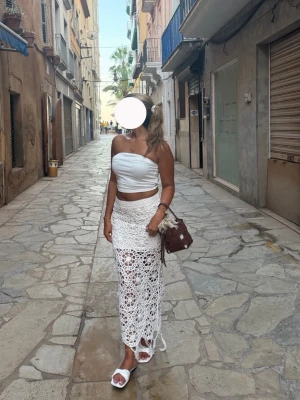 Vit lång virkad kjol med slits - Säljer en superfin långkjol i vit virkad stil med snygg. Kjolen har ett genombrutet mönster som ger en luftig och somrig känsla. Perfekt att styla med crop top eller bikini. Resår i midjan för skön passform.