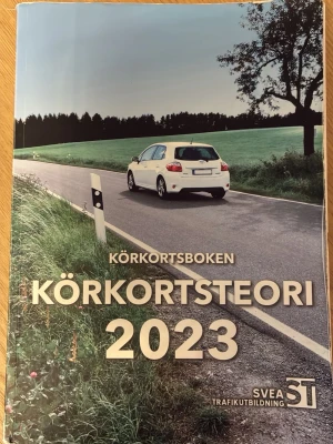 Körkortsteori 2023 Svea Trafikutbildning - Körkortsboken 'Körkortsteori 2023' från Svea Trafikutbildning är en komplett teoribok för dig som ska ta B-körkort. Boken är tryckt i färg, har mjuka pärmar och innehåller tydliga bilder och uppdaterad information enligt Transportstyrelsens kursplan.                         Bokens omslag är slitet, men insidan är helt fri från anteckningar och är fullt läsbar.