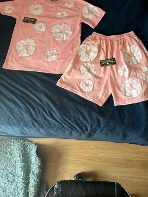Denmin tears set  - Säljer ett denmin tears set med t-shirt och shorts, dekorerat med vita blommönster över hela plaggen. Båda delarna har en svart etikett med text framtill. Setet har avslappnad passform och är gjort i mjukt bomullsliknande material.