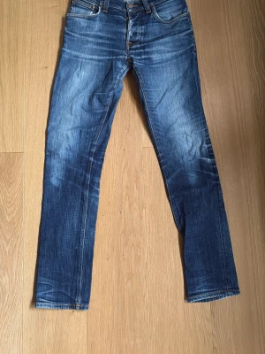 Nudie Jeans Grim Tim Dry Open Navy- W31 L34 - Nudie Jeans Grim Tim Dry Open Navy - W31 L34.  Bra skick. Fina naturlig patina. Skrev lagat hos Nudie Jeans i Göteborg. Båda framfickorna lagade samt pyttelitet hål lagat på insidan vänsterbenet mot sömmen hos Nudie Jeans i Stockholm.  98% bomull 2% stretch  Kontakta mig gärna för frågor och för prisförslag. Midja 39 cm Längd 104 cm Innerbenslängd 80 cm