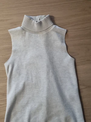 Stickad polotopp från Zara - Säljer en ljus, stickad polotopp från Zara. Toppen är ärmlös med hög, ribbad polokrage och har en mjuk, bekväm känsla. Perfekt att styla med jeans eller kjol för en clean look.