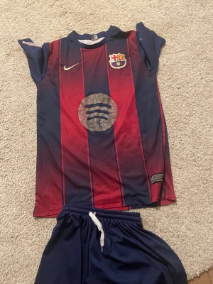 FC Barcelona Lamine Yamal tröja 170cm - Säljer en FC Barcelona matchtröja med Lamine Yamal och nummer 19 på ryggen. Tröjan är kortärmad, har klassiska blå och röda ränder, Nike-logga och Spotify som sponsor på bröstet. Materialet är lätt och andas, perfekt för fotbollsträning eller match.