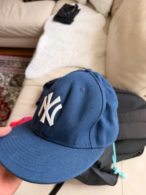 Blå New York Yankees keps - Snygg blå keps med klassisk New York Yankees-logga broderad i vitt framtill. Kepsen har böjd skärm och är tillverkad i ett slitstarkt tygmaterial. MLB-logga broderad baktill för extra stilpoäng.