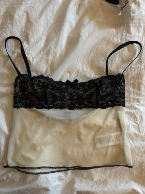 Svart spetsbody med meshdetaljer - Säljer en snygg body med svarta spetskupor och tunna axelband. Nedre delen är i transparent vit mesh som ger en modern och luftig känsla. Perfekt för dig som gillar trendiga underkläder med fina detaljer.