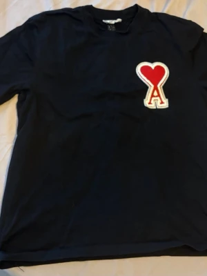 Svart t-shirt med rött hjärta - Snygg svart t-shirt med ett stort rött hjärta och bokstaven A broderat på bröstet. Klassisk rund hals och korta ärmar. Perfekt för dig som vill ha en enkel men ändå unik look.