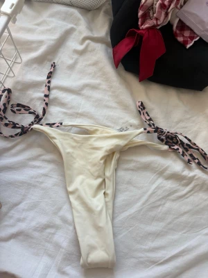 Vit string bikiniunderdel - Säljer en vit bikiniunderdel med string och knytband i leopardmönster. Snygg och trendig modell som ger en fräsch look på stranden. Perfekt för dig som vill ha något unikt och stilrent till sommaren.