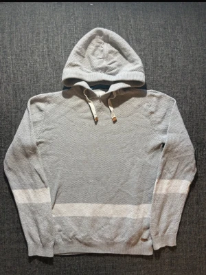 Ljusgrå hoodie från edc  - Snygg ljusgrå hoodie med vita ränder på ärmar och nederkant. Tröjan har huva med dragsko och är tillverkad i ett mjukt, stickat material. Perfekt för en avslappnad och stilren look.