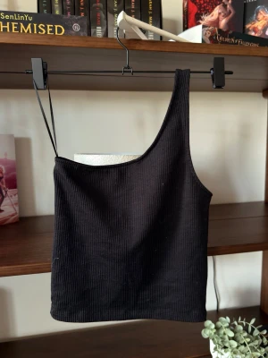 Oneshoulder topp || Gina Tricot - Säljer en svart ribbad oneshoulder topp från Gina Tricot i storlek XS. Toppen har en asymmetrisk axel med ett smalt band på ena sidan och är tillverkad i mjukt, stretchigt material. ÄLSSKARR.                                ⭐️Säljes i använt skick, utan defekter & slitage. Väl omhändertagen                                                                             💭Har du frågor? Skriv på annonsen och jag svarar så fort jag kan!