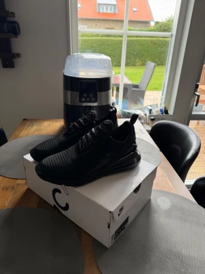 Nike Air Max 270 helsvarta sneakers - Snygga helsvarta Nike Air Max 270 sneakers med mesh-ovandel och stor synlig Air-enhet i hälen. Skorna har en sportig siluett, klassisk snörning och diskreta detaljer. Perfekta för dig som gillar stilrena och bekväma sneakers.
