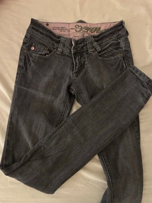 Mörkgrå skinny jeans med broderi - Snygga mörkgrå skinny jeans med dekorativa broderier på bakfickorna och rosa detaljer på knapparna. Jeansen har klassisk femficksmodell och låg midja. Perfekta för dig som gillar en trendig och stilren look.