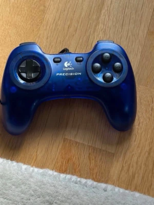 Blå Logitech Precision handkontroll - Classic Logitech Precision Gamepad in a cool translucent dark blue design with black buttons and directional pad.  • Brand: Logitech • Model: Precision Gamepad • Connection: Wired USB • Compatible with PC/Mac • Great for retro gaming, emulators and classic PC games • Translucent blue plastic shell • Comfortable, classic controller design  Condition: Barely used and in very good condition.  Store price was around 400 SEK.